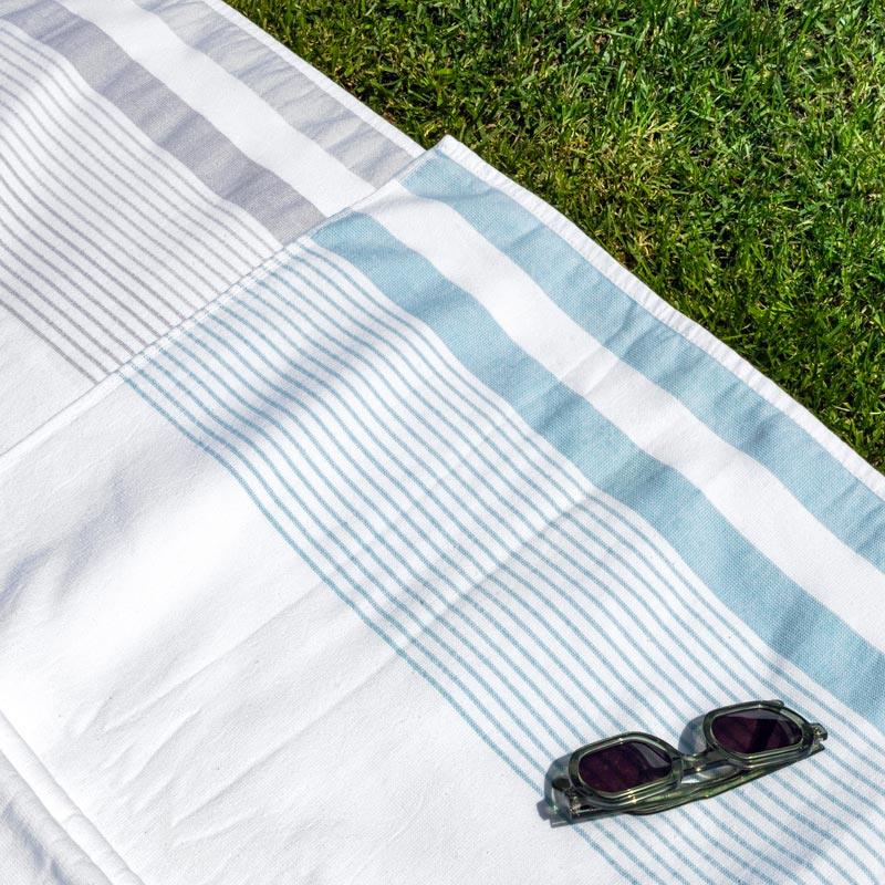 Striped white, grey, and blue peshtemal towel on grass with sunglasses