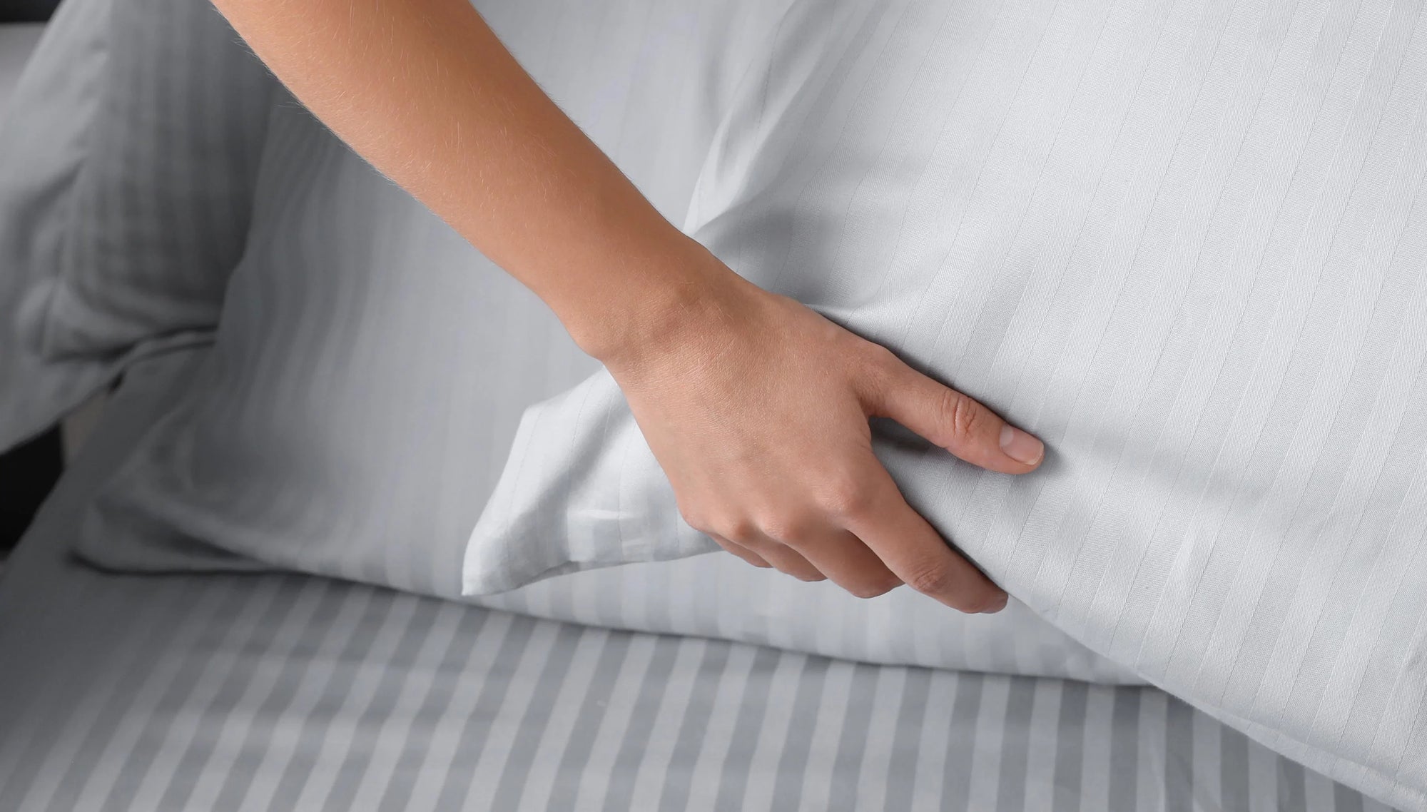 Hand touching white striped pillow on matching striped bed sheets